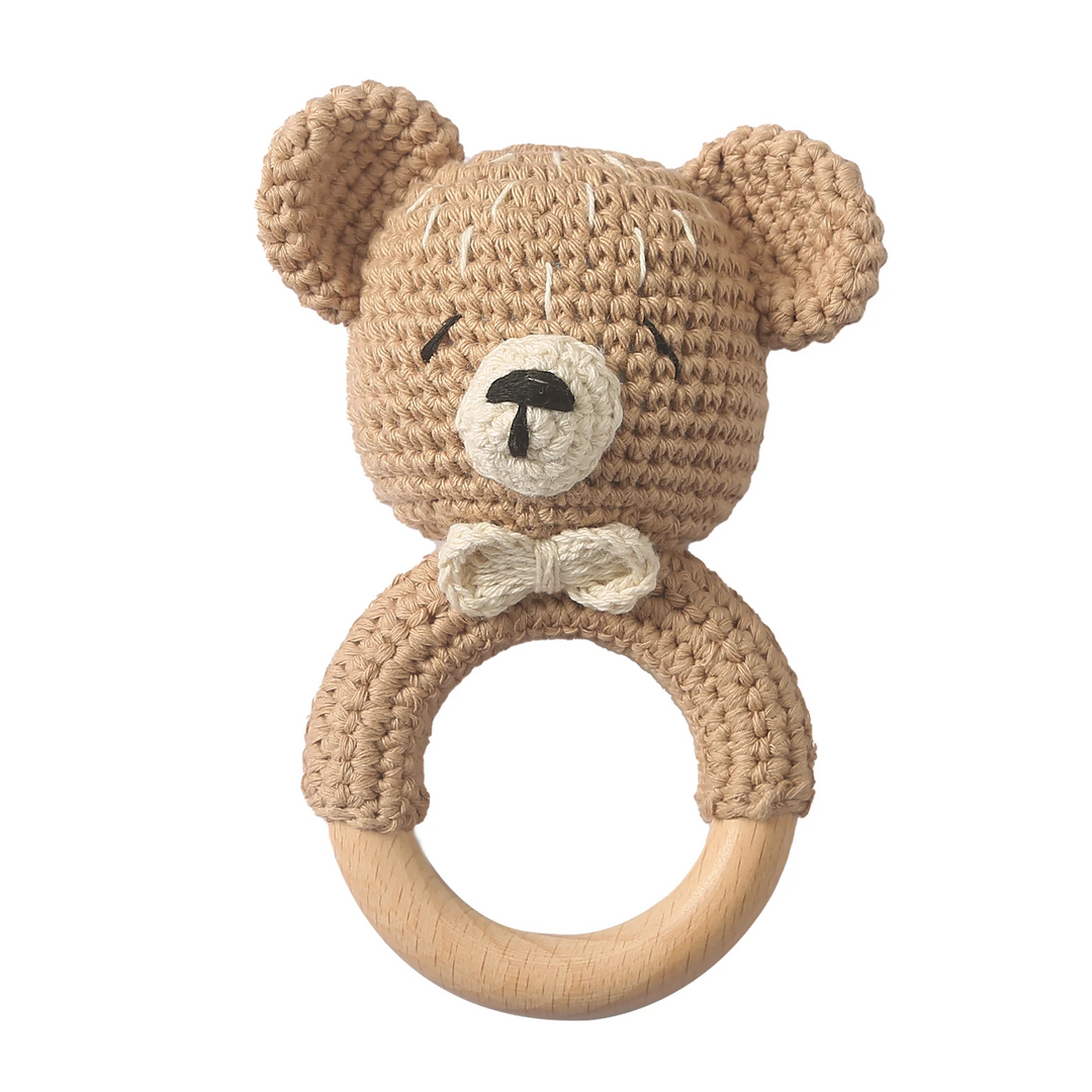 Beige crocheted bear rattle with a light bow and natural wooden ring