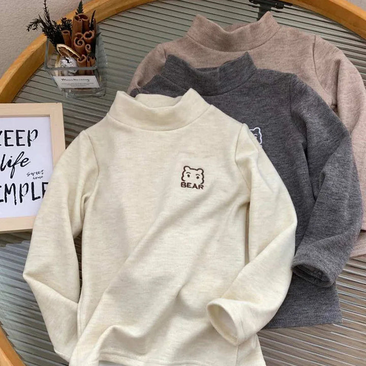 Beige high-neck bear shirt displayed in front of dark gray and khaki shirts