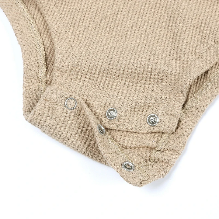 Bottom snap fastening on a beige ribbed baby bodysuit