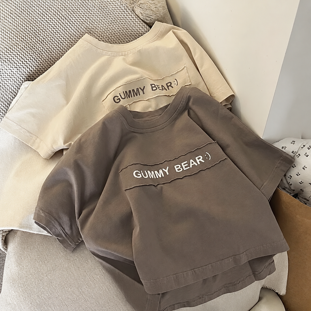 Beige and brown boys' T-shirts with Gummy Bear lettering arranged on a cushioned chair