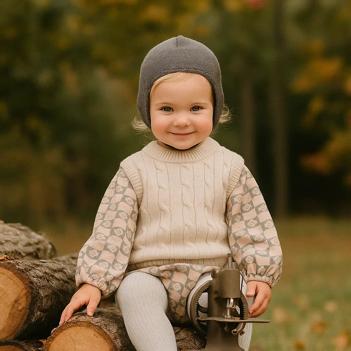 Toddler outdoors wearing a beige cable-knit vest over a patterned shirt