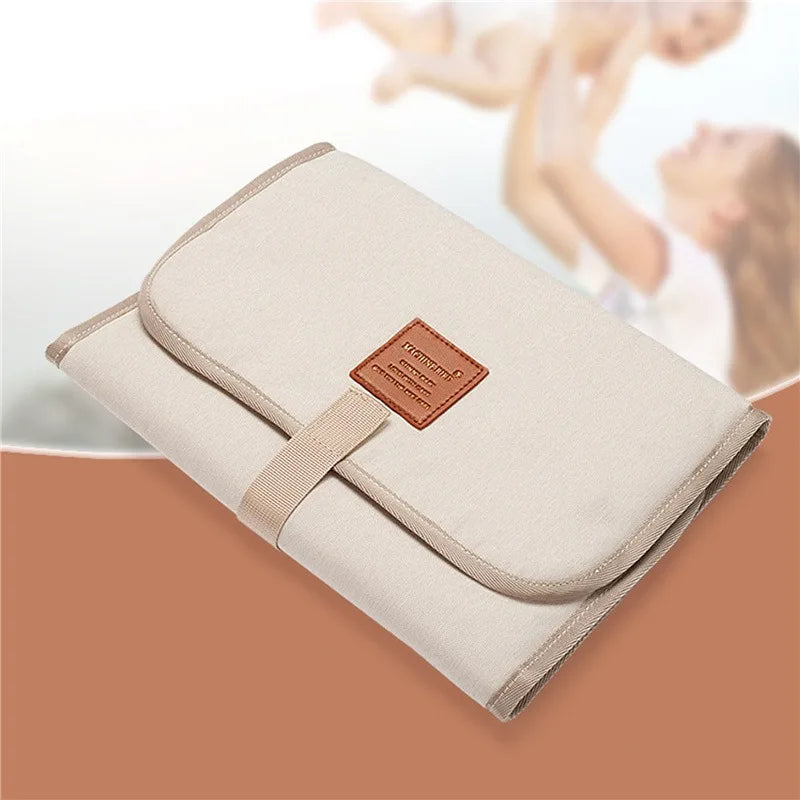 Beige changing mat folded with a front strap, with a parent and baby in the background
