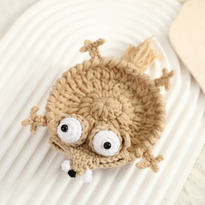 Beige Coyote coaster with large white eyes, a pointed snout, and small crocheted paws