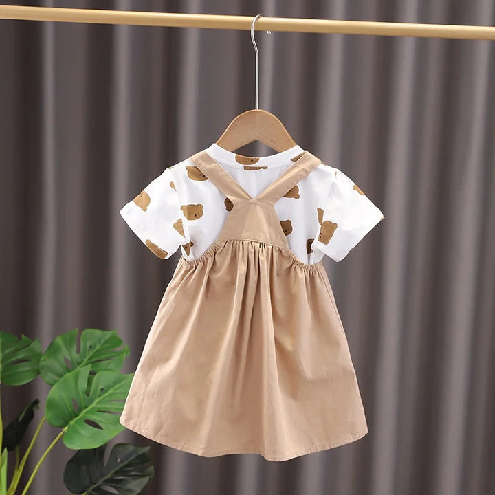 Back of a beige overall dress with crossed straps over a white bear-print T-shirt