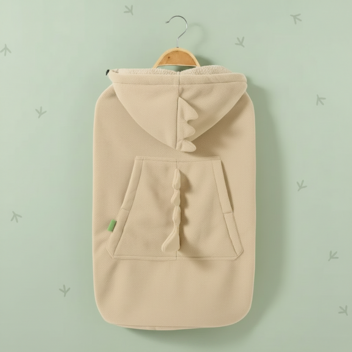 Beige dinosaur baby carrier cover hanging from a hanger with raised spikes on the hood and pocket