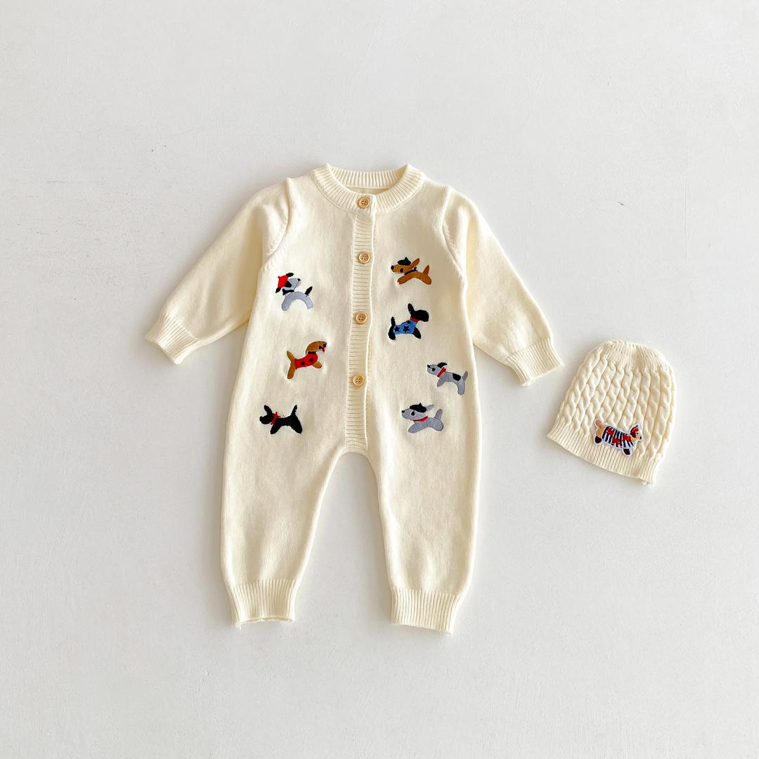 Beige dog-pattern knitted baby jumpsuit laid flat beside a beige knit hat