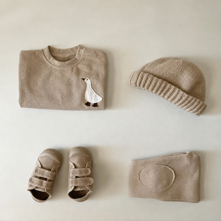 Folded beige goose sweater and knee-detail pants styled with a knit hat and sandals