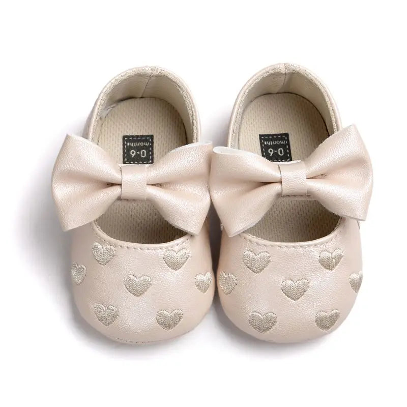 Beige baby shoes with matching bows and heart details, viewed from above
