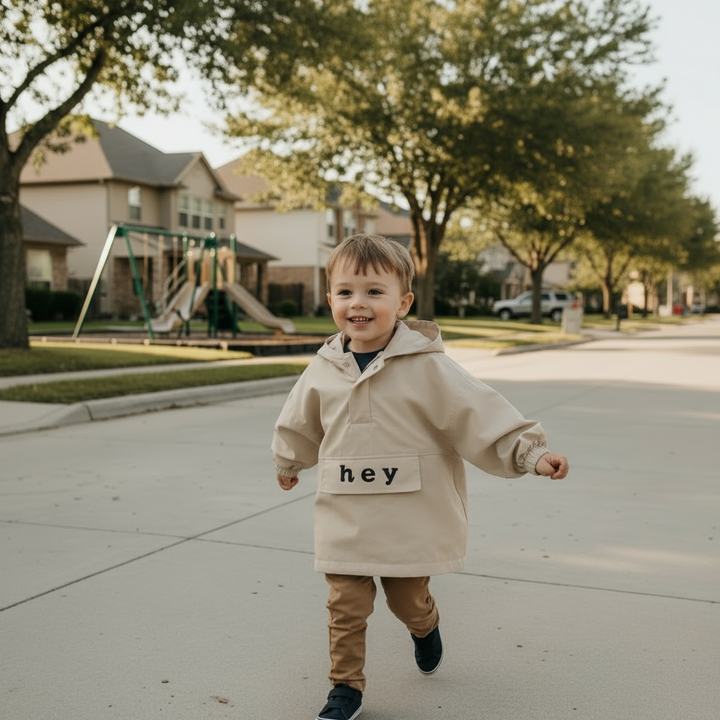 Child wearing a beige hooded windbreaker while walking along a neighborhood sidewalk