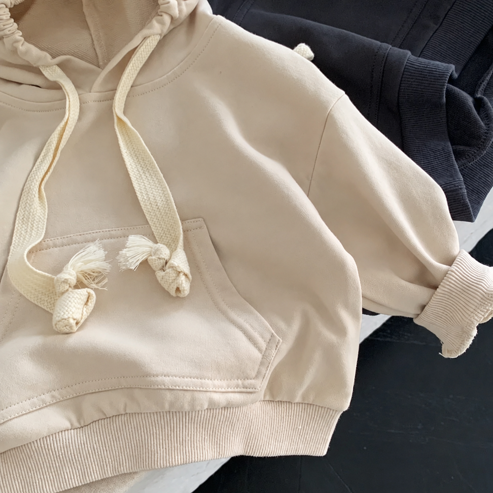 Close-up of a beige kids' hoodie showing the front pocket, knotted drawstrings, and ribbed hem
