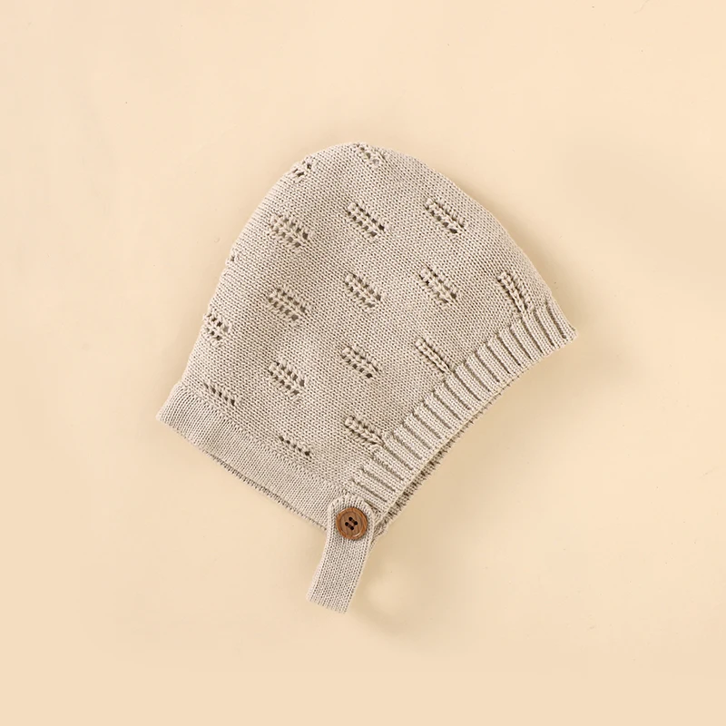 Beige knitted baby hat showing the patterned knit, ribbed edge, and button tab.