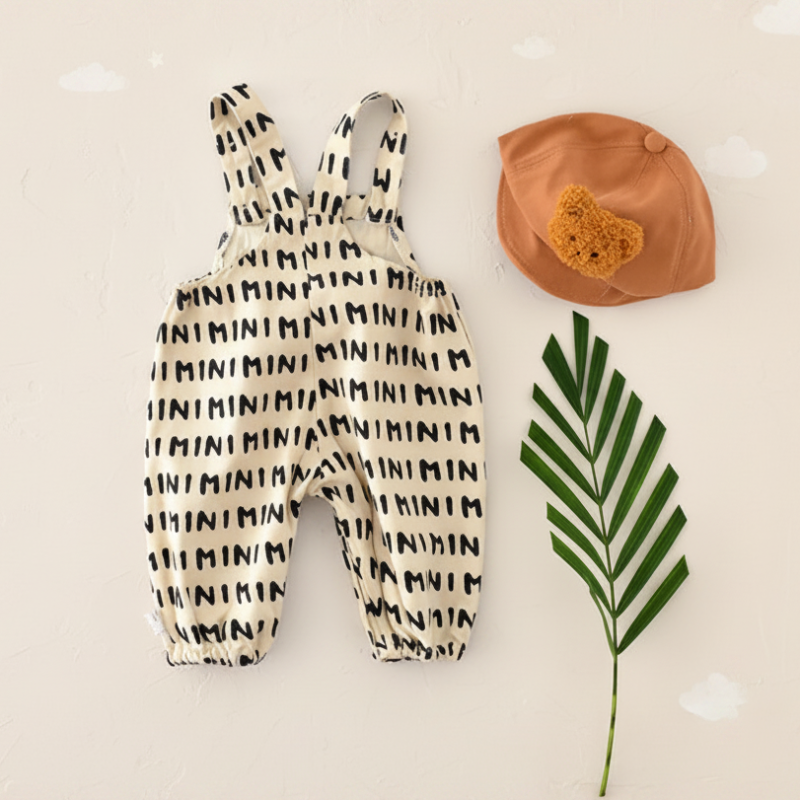 Beige MINI-print overall romper laid flat beside a brown hat
