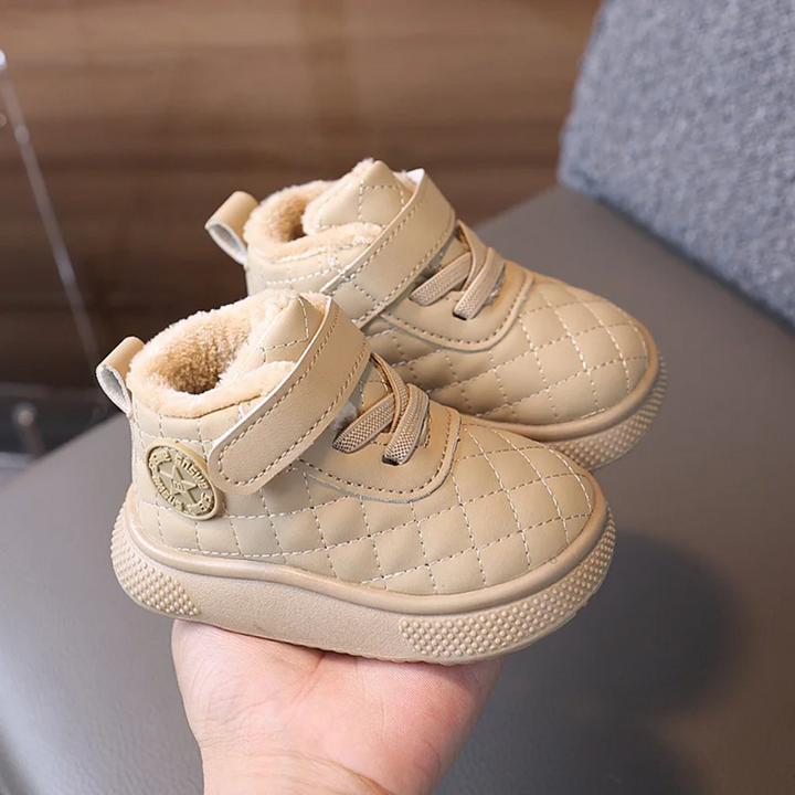 Pair of beige quilted winter boots with ankle straps held in one hand