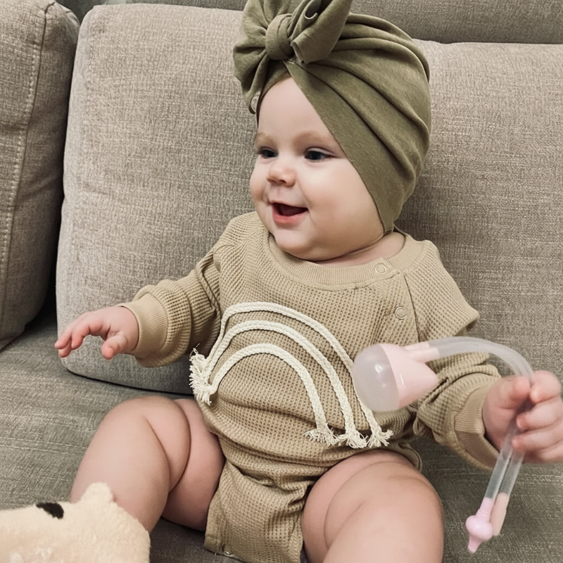 Baby wearing a beige textured rainbow bodysuit while sitting on a gray sofa