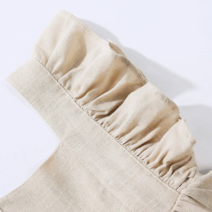 Close-up of the gathered ruffle along a beige romper shoulder strap.
