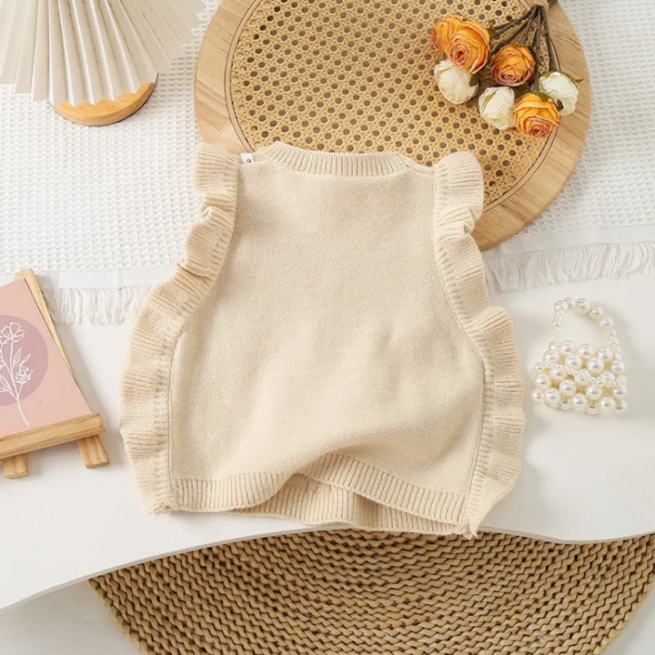Back of the beige knit vest showing a plain knit panel, ribbed hem, and ruffled armholes