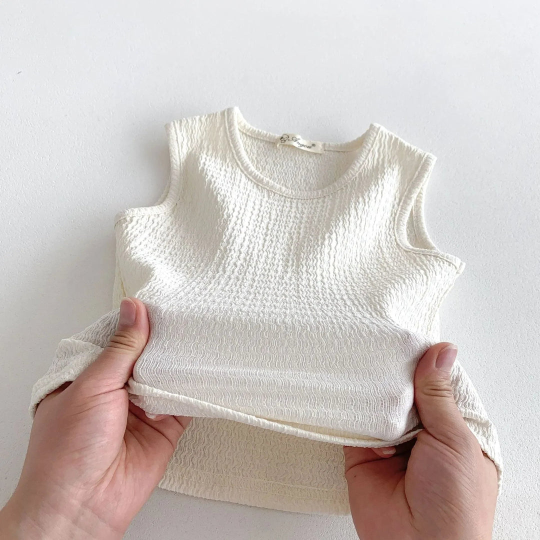 Hands holding a beige sleeveless cotton top to show its textured fabric.