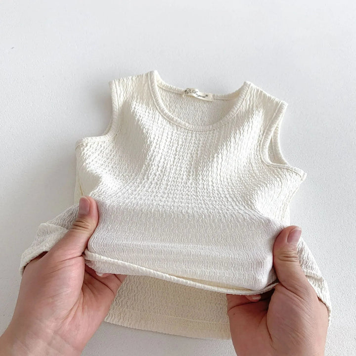 Hands holding a beige sleeveless cotton top to show its textured fabric.
