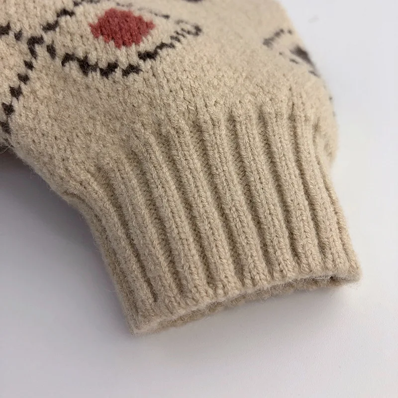 Close-up of the ribbed sleeve cuff and small red diamond on the beige sweater