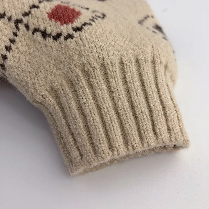 Close-up of the ribbed sleeve cuff and small red diamond on the beige sweater