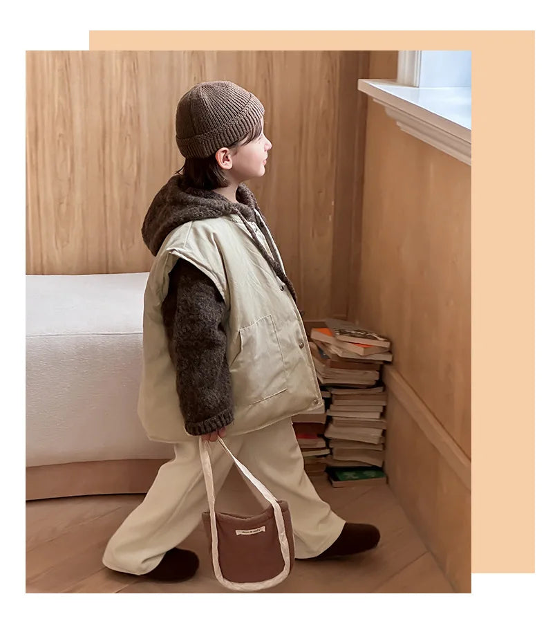Side view of a child wearing a beige vest over a brown knit hoodie indoors.