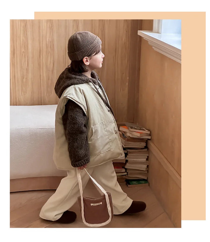 Side view of a child wearing a beige vest over a brown knit hoodie indoors.