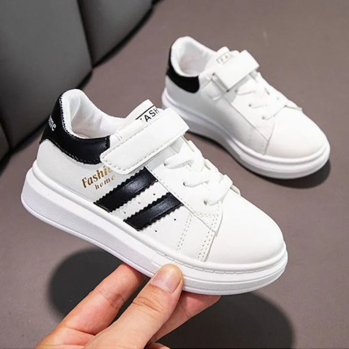 White sneakers with black stripes, with one shoe held to show the side and strap.