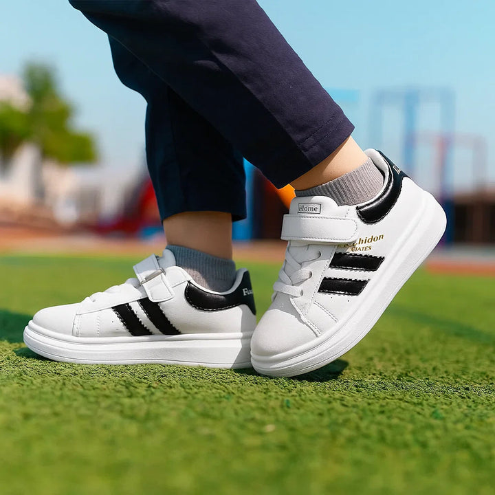 Child wearing white sneakers with black accents and strap closures on grass.