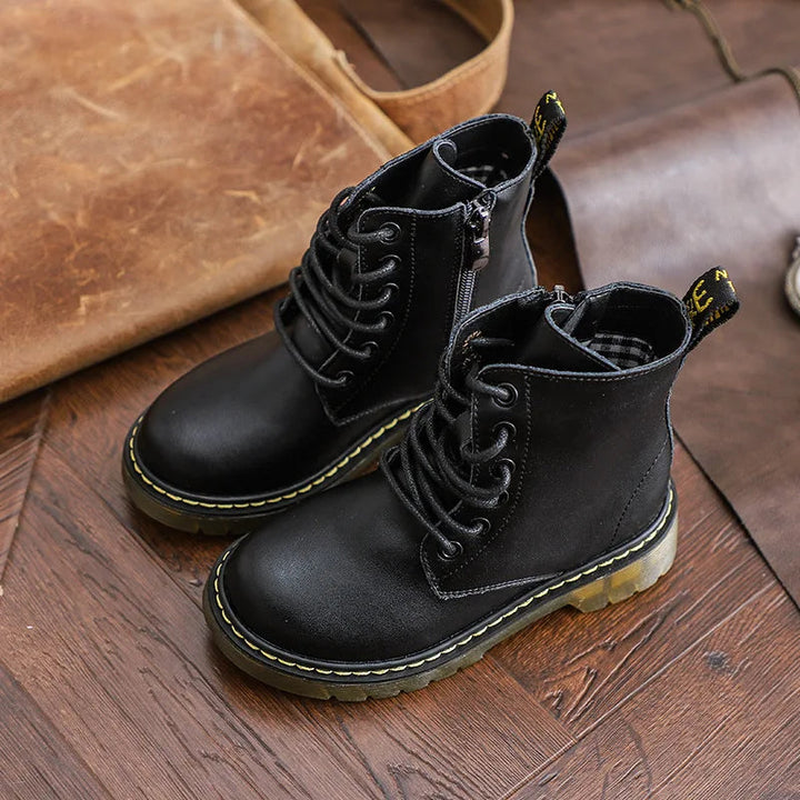 Black ankle lace-up boots with side zippers and translucent soles on a wooden floor