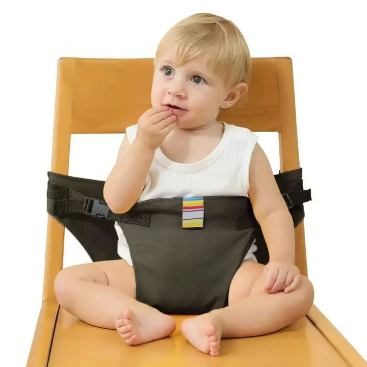 Front view of a child seated on a wooden chair wearing the black harness.