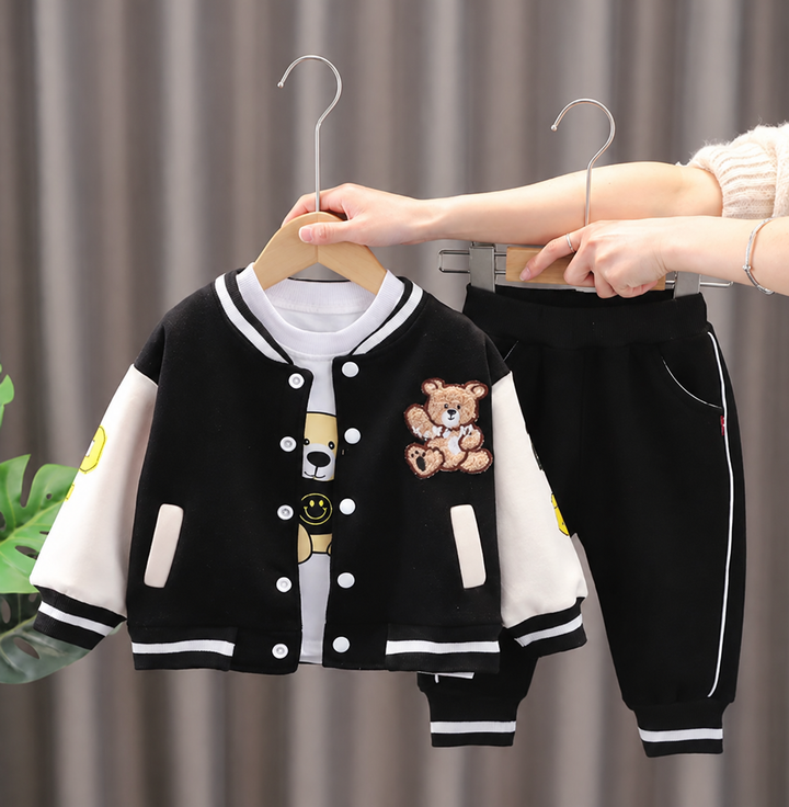 Black-and-white bear-patch varsity jacket, graphic T-shirt, and matching black pants on hangers