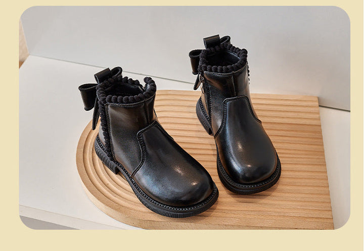Pair of black ankle boots with back bows and decorative trim on a wooden display