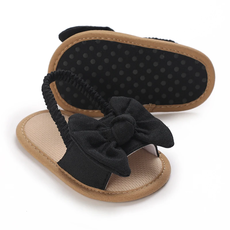 Black bow baby sandals showing the dotted sole and elastic heel strap
