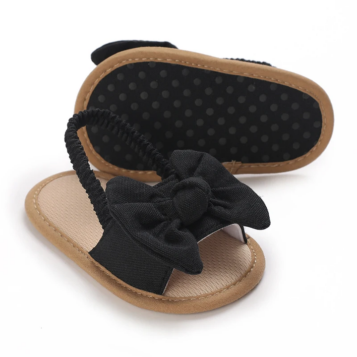 Black bow baby sandals showing the dotted sole and elastic heel strap