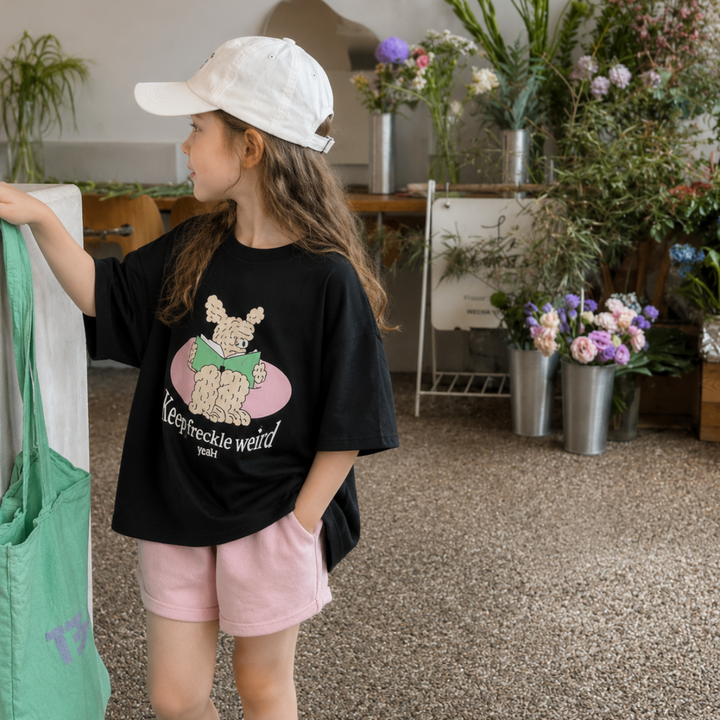 Girl in a black cartoon-print T-shirt and pink shorts, shown in side view