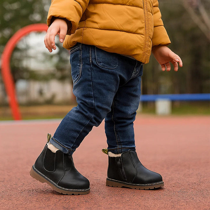 Child wearing black Chelsea boots with jeans and a mustard-colored jacket on a playground