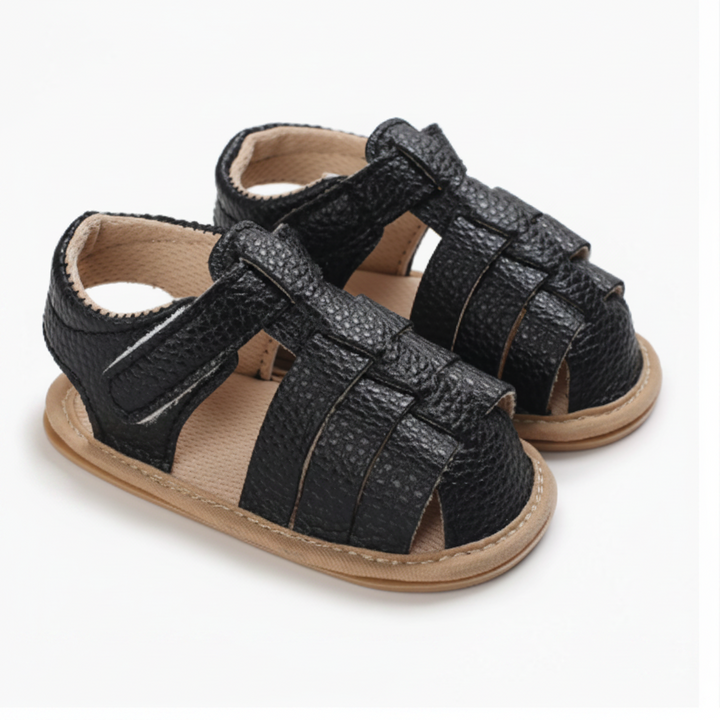 Pair of black closed-toe baby sandals with interwoven straps and ankle fastenings