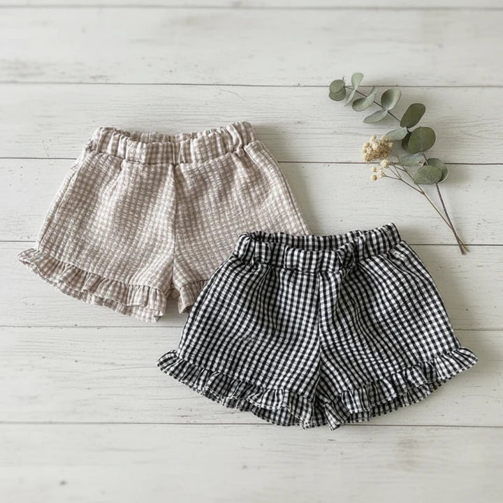 Black and Coffee gingham bloomers with ruffled hems laid flat on white wooden boards