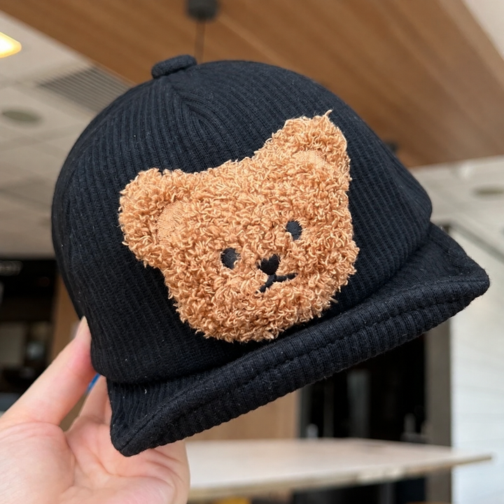 Black corduroy baby cap held to show the fuzzy brown bear face and brim
