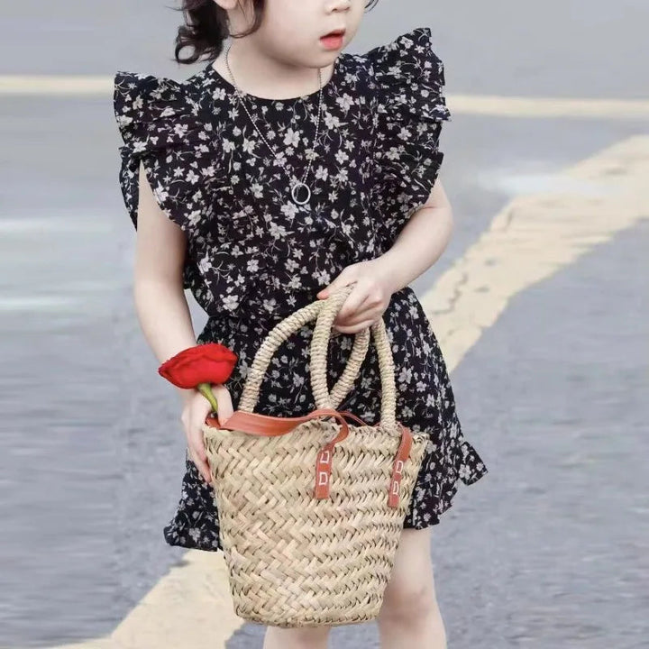 Child wearing a black floral ruffle-sleeve top and matching shorts outdoors, holding a woven basket
