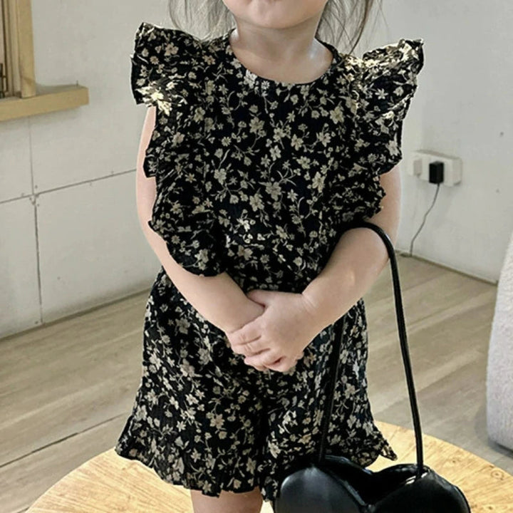 Black floral top and matching ruffle-hem shorts worn indoors with a black handbag