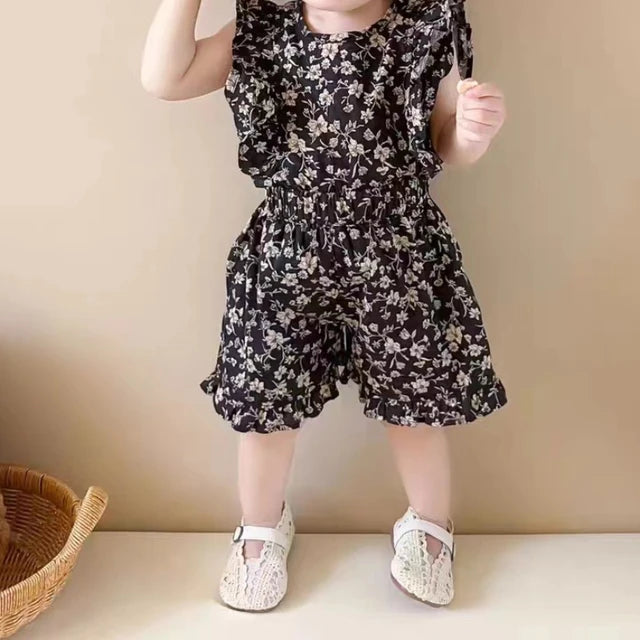 Child modeling the black floral ruffle-sleeve top and shorts with white shoes