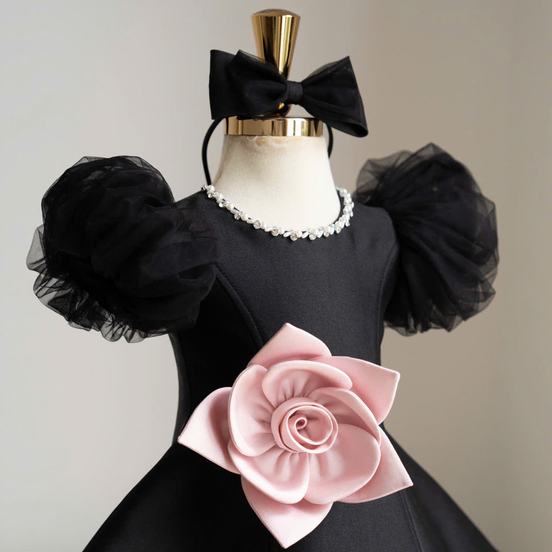Black dress close-up showing sheer puff sleeves, a pink flower and decorative neckline