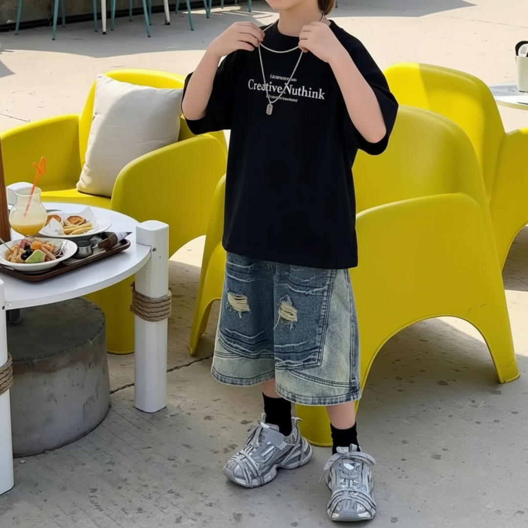 Boy wearing a black short-sleeve graphic T-shirt with distressed denim shorts