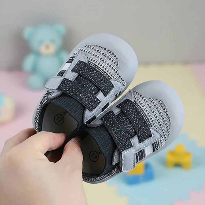 A pair of black-gray mesh baby shoes held by their heel openings