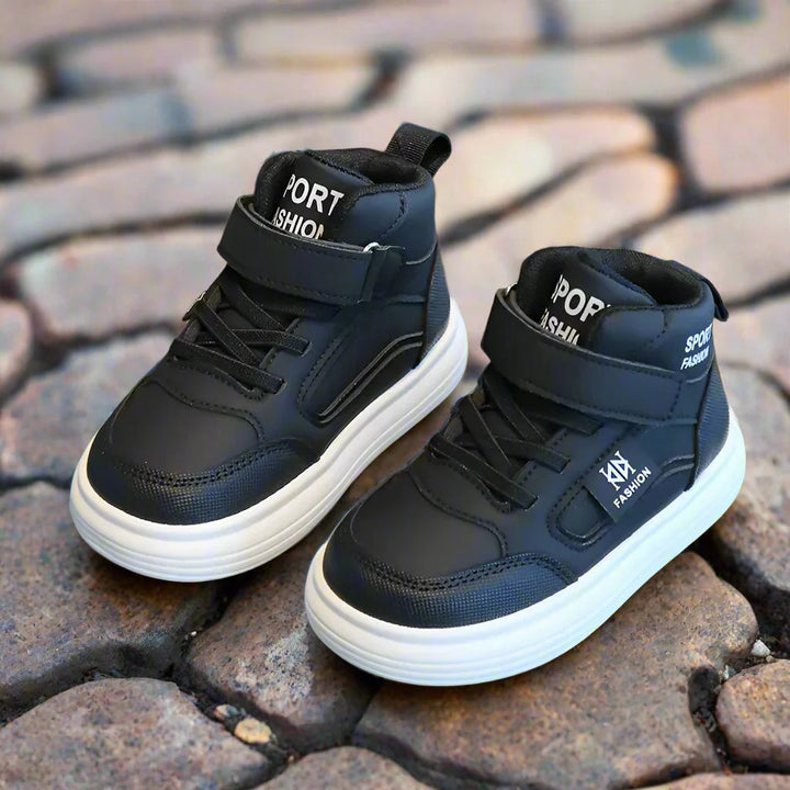 Pair of black high-top sneakers with ankle straps and white soles on cobblestones