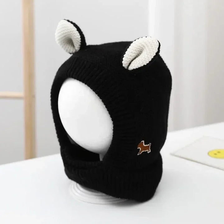 Black knit balaclava with cream ears, ribbed face trim, and a small animal patch