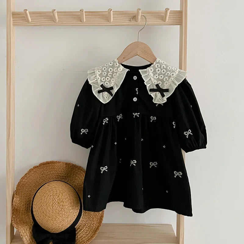 Black dress with a cream lace collar and embroidered bows hanging from a wooden rack