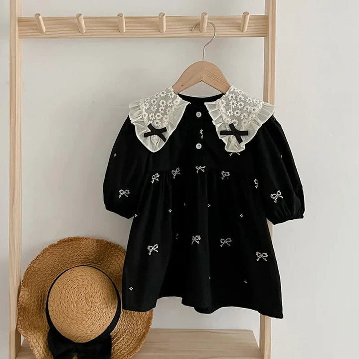 Black dress with a cream lace collar and embroidered bows hanging from a wooden rack