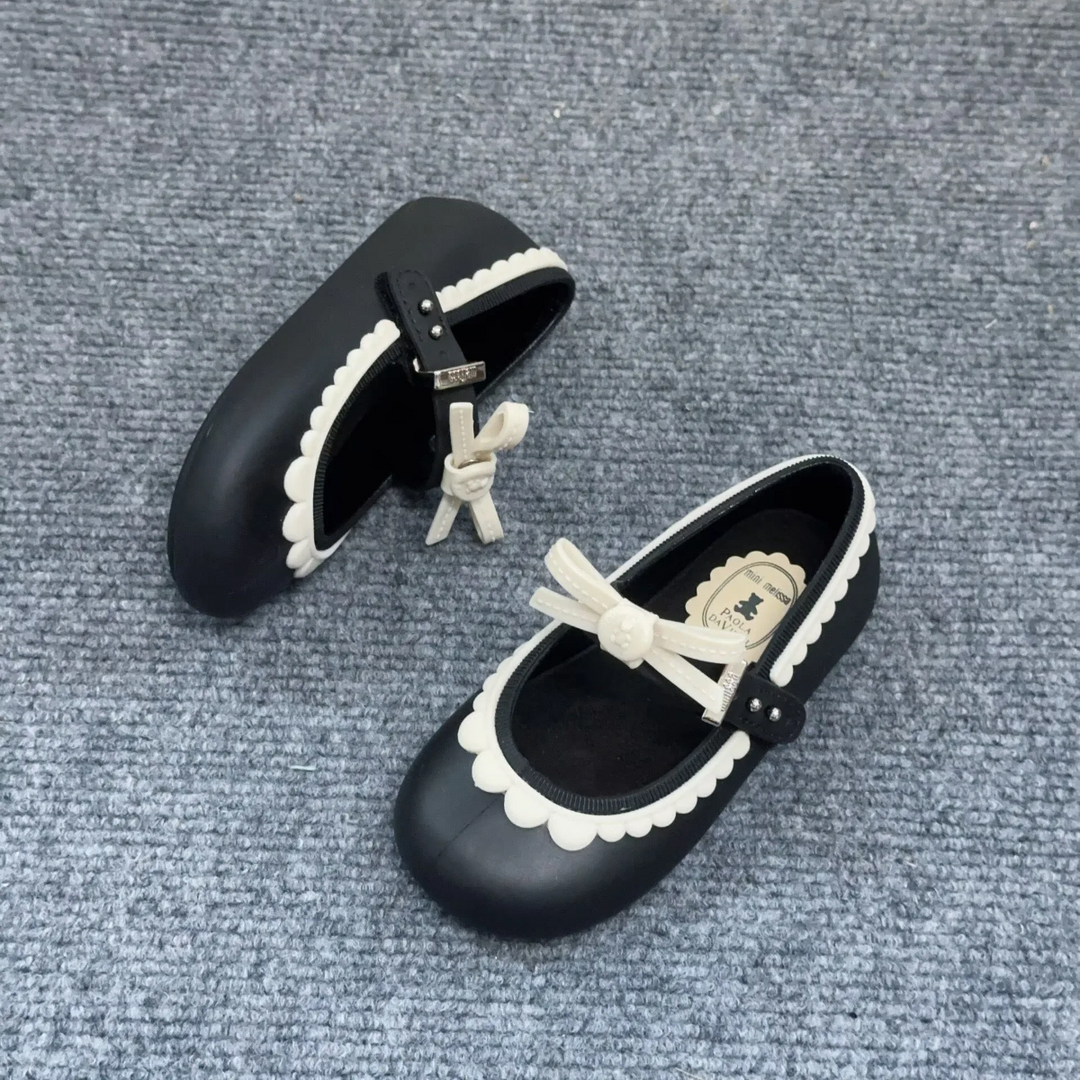 Overhead view of black Mary Jane shoes with white bows, scalloped trim, and adjustable straps